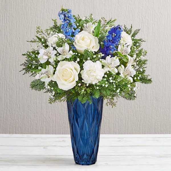 White roses and blue flowers arranged in a tall blue vase