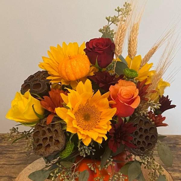Autumn bouquet with sunflowers, roses, and wheat in an orange pumpkin vase