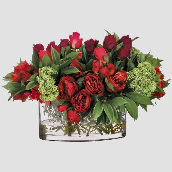 Red roses and red tulips arranged in a clear glass vase