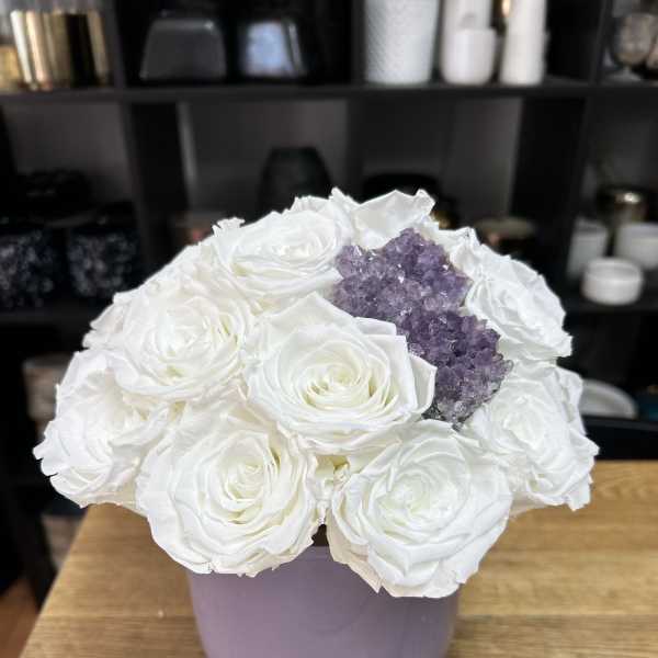 White roses arranged in a lavender vase with a purple crystal cluster