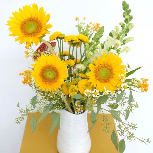 Yellow sunflower bouquet in a white vase with mixed small blooms