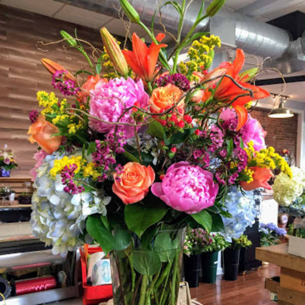 Tall mixed bouquet in a clear glass vase with lilies, roses, peonies, and hydrangeas