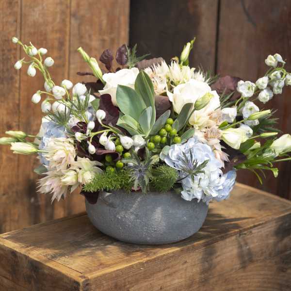 Mixed floral arrangement in a gray bowl vase with white and pale blue blooms