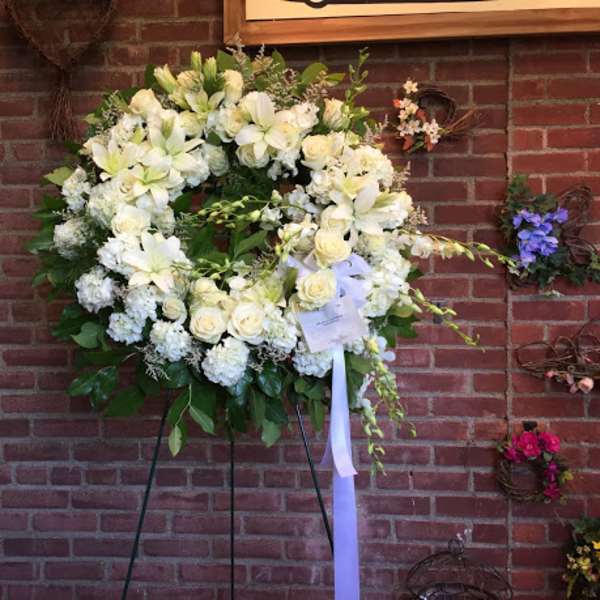 Large white floral wreath on a stand with a ribbon