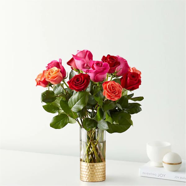 Tall glass vase with pink, red, and orange roses on a white surface