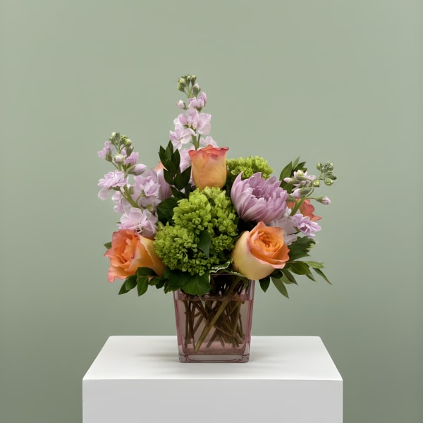 Mixed bouquet of peach roses, lavender blooms, and green flowers in a pink vase