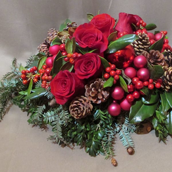 Low arrangement of red roses with red berries, pinecones, and red ornaments in a holiday centerpiece