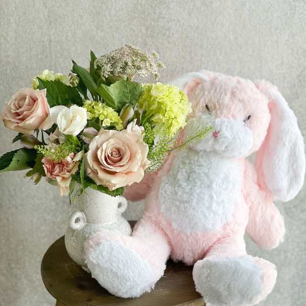 Pink plush bunny beside a vase of pale roses and mixed flowers