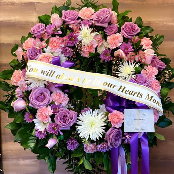 Heart-shaped floral wreath with purple and pink flowers and a memorial ribbon
