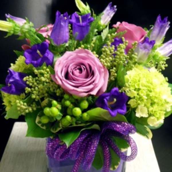 Pink and purple bouquet in a square glass vase with a purple ribbon