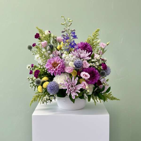 Mixed bouquet of pink, purple, white, and yellow flowers in a white bowl vase