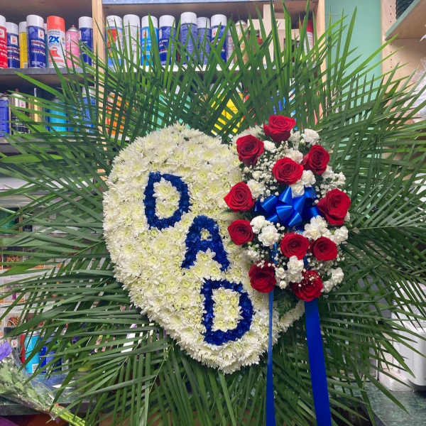 Heart-shaped floral tribute with white flowers, red roses, and blue letters
