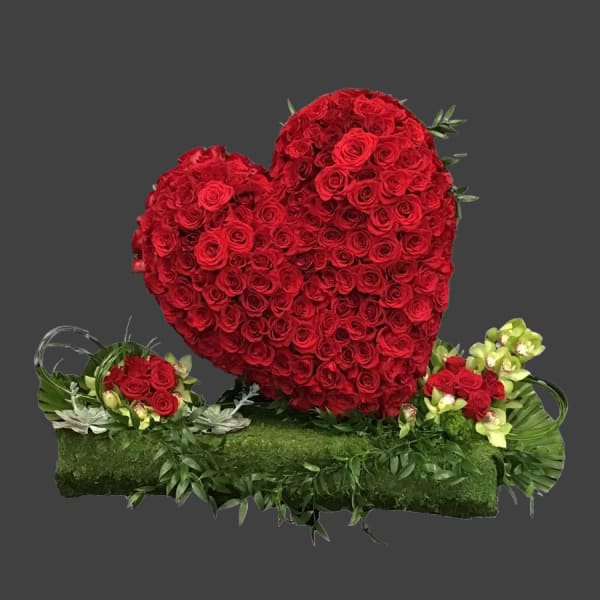 Heart-shaped red rose arrangement on a green base with small side bouquets