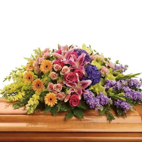 Colorful floral casket spray with pink lilies, roses, and purple blooms