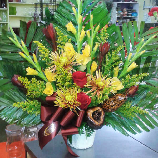 Tropical bouquet with yellow flowers, red roses, and large palm leaves in a white vase