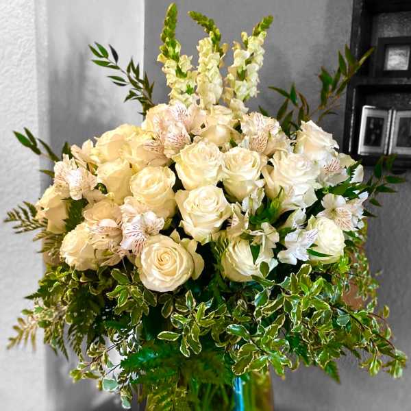 Cream roses and white flowers in a glass vase with greenery