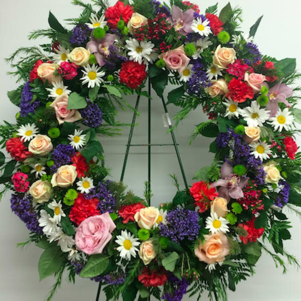 Large floral wreath on an easel with roses, daisies, and mixed blooms