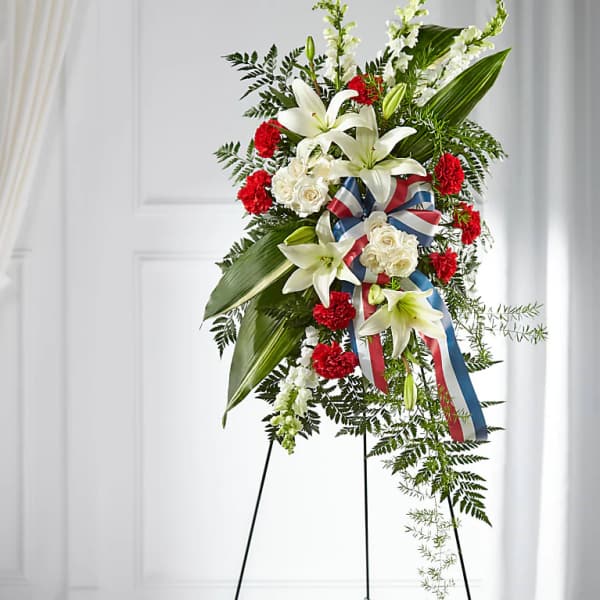 Standing floral spray with white lilies, red carnations, and a patriotic ribbon