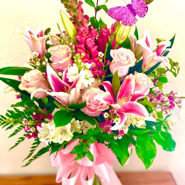 Pink roses and lilies in a glass vase with a pink ribbon and butterfly pick