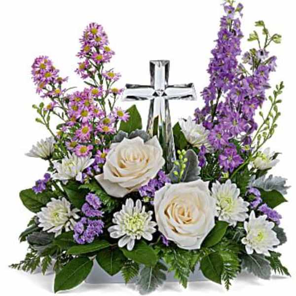 White roses and purple flowers arranged around a clear glass cross