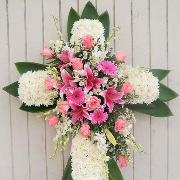 Standing cross-shaped funeral spray of white mums with pink lilies, roses, and gerbera daisies.