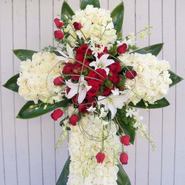 Standing cross of white flowers with red roses and white lilies on an easel