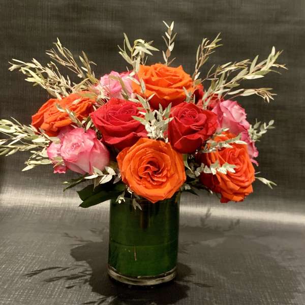 Bouquet of red, orange, and pink roses in a green glass vase