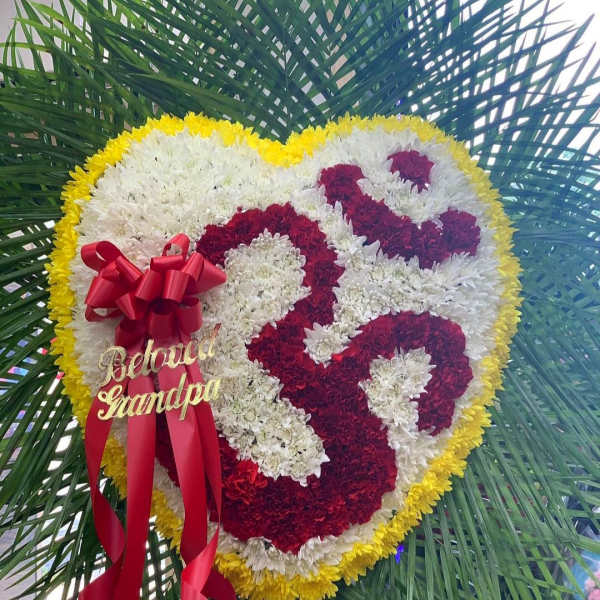 Heart-shaped floral tribute with red, white, and yellow flowers and a red ribbon