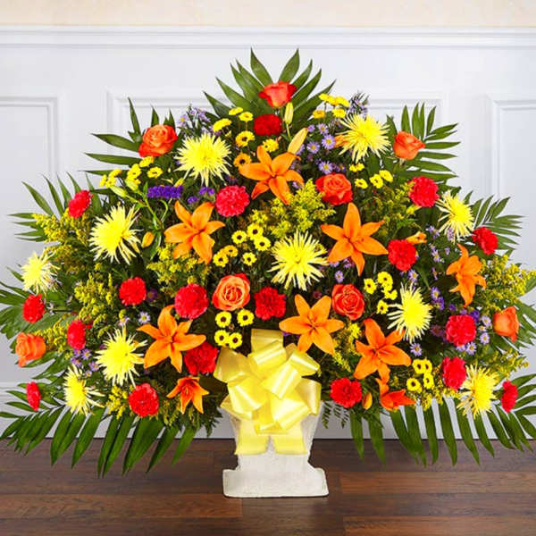 Large colorful floral spray with orange lilies and roses in a white pedestal vase