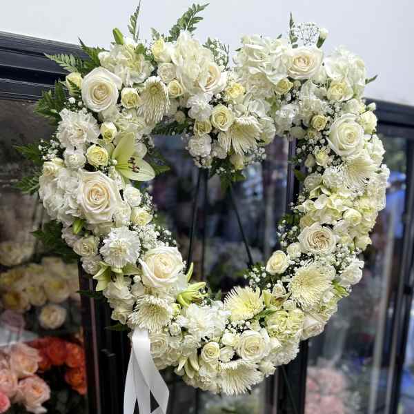 Heart-shaped white floral wreath with a white ribbon bow