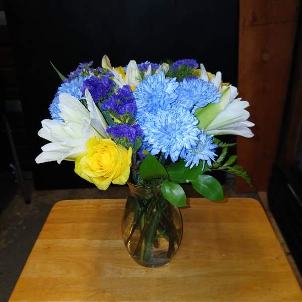 Mixed bouquet of blue, white, yellow, and purple flowers in a glass vase