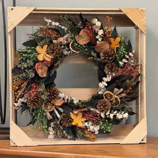 Rustic wreath with pinecones, dried orange slices, and orange flowers in a wooden frame