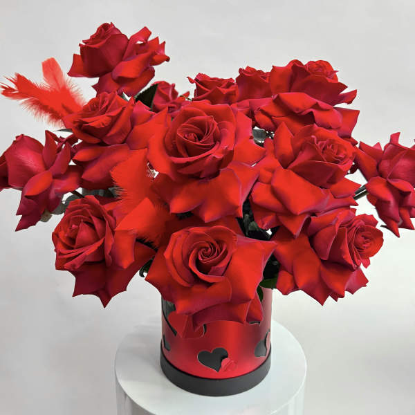 Red roses arranged in a heart-decorated black vase with red feathers
