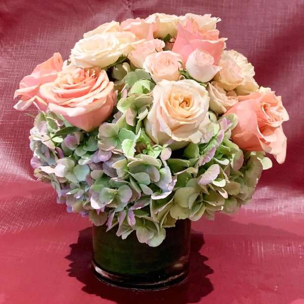 Pink and cream roses arranged with hydrangeas in a dark vase