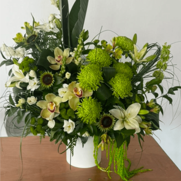 Green and white floral arrangement in a white vase with orchids and lilies