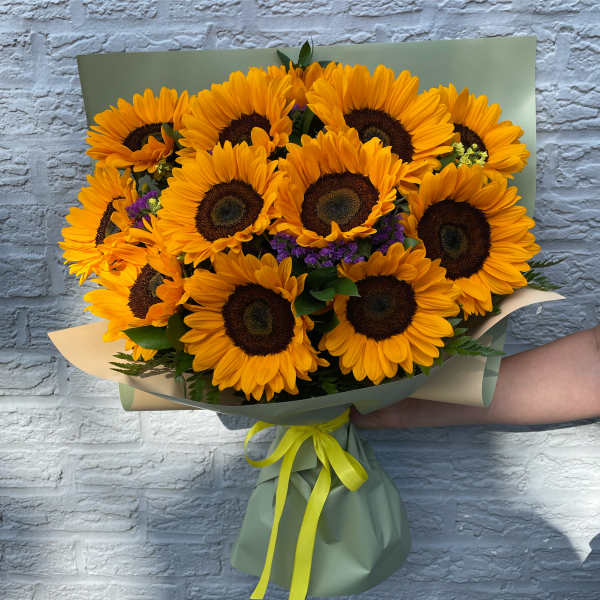 Bouquet of bright yellow sunflowers wrapped in green paper with a yellow ribbon