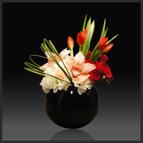 Bouquet of red roses and peach orchids in a black vase