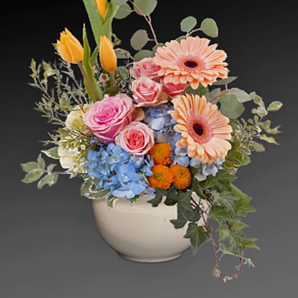 Mixed bouquet of pink, peach, blue, and orange flowers in a white vase
