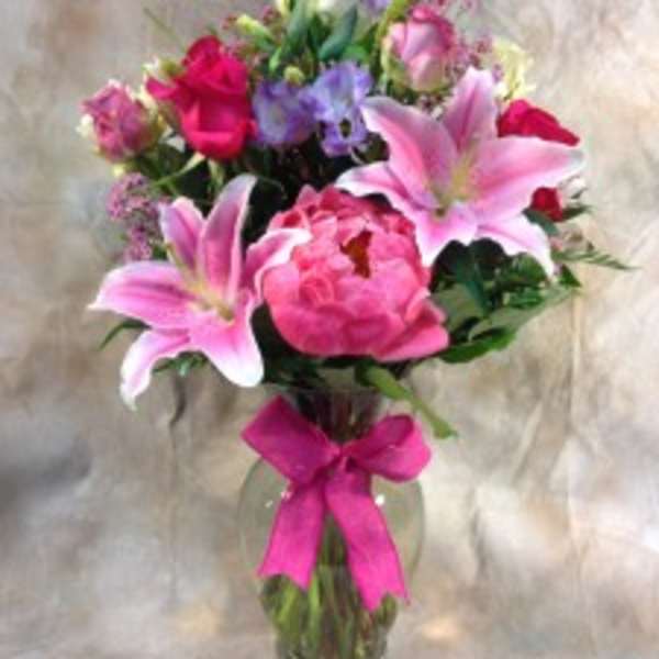 Pink lilies and roses in a glass vase with a bright ribbon