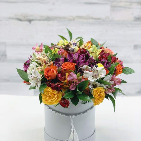 Mixed bouquet of orange, yellow, pink, and white flowers in a gray hat box