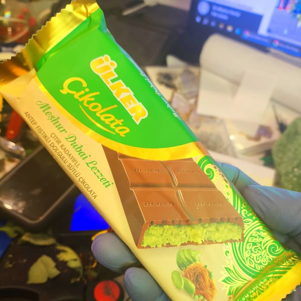 Hand holding a wrapped chocolate bar with green and gold packaging