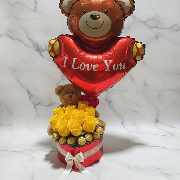 Teddy bear balloon above yellow roses in a red gift box