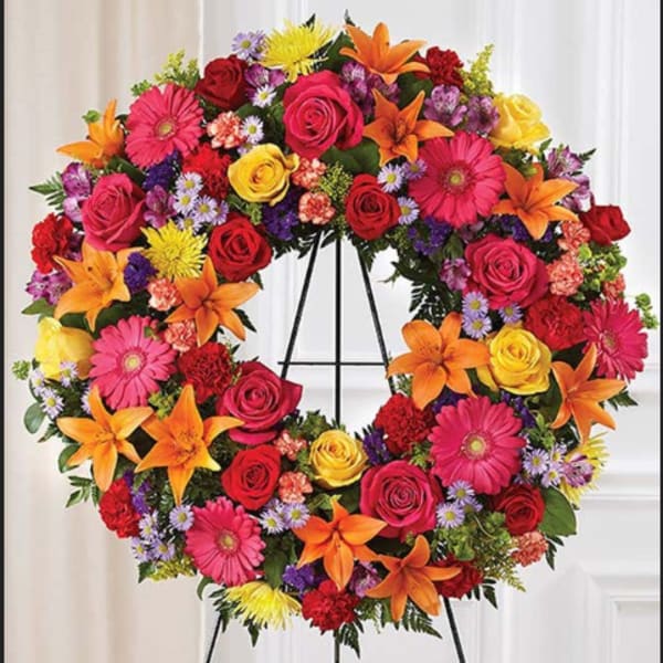 Colorful floral wreath on a black stand with roses, lilies, and daisies