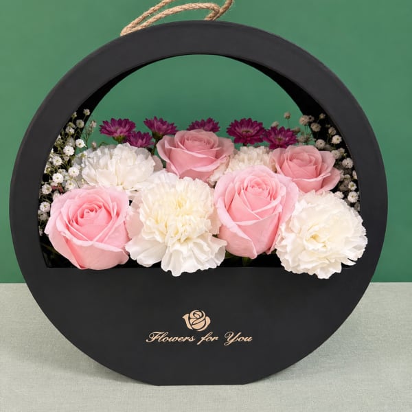 Pink roses and white carnations arranged in a round black gift box