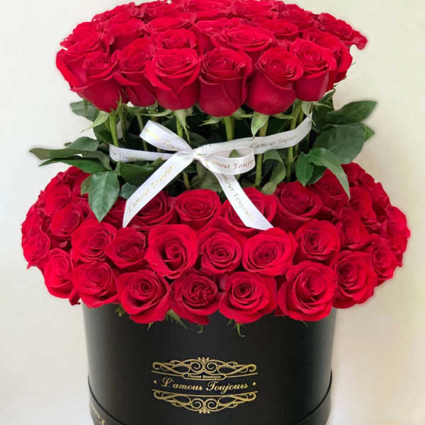 Two-tier arrangement of red roses in a round black hatbox with white ribbon