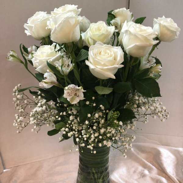 White roses and small white filler flowers in a tall glass vase