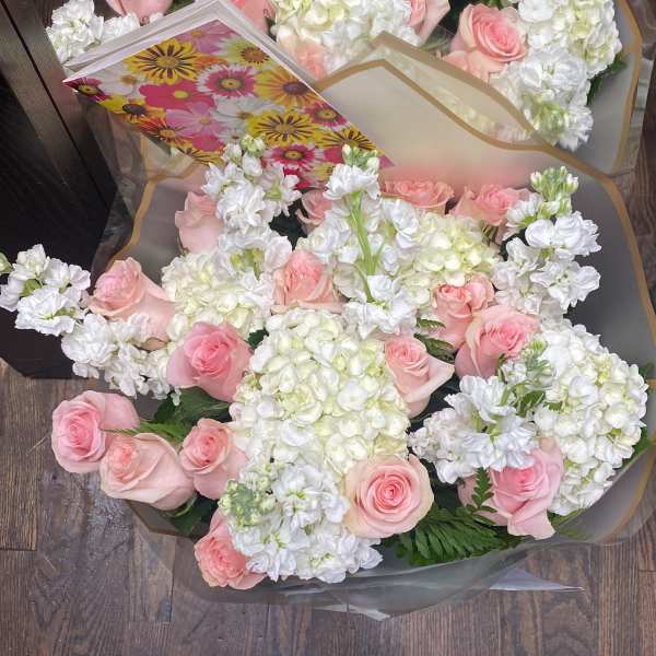 Two bouquets of pink roses and white flowers wrapped in clear paper