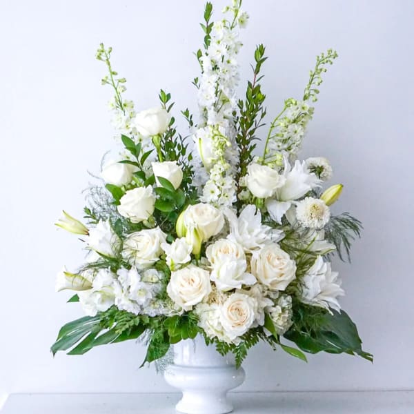 White roses and lilies arranged in a white urn vase