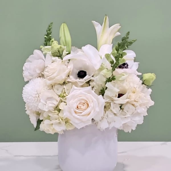 White floral arrangement in a white vase with lilies and roses