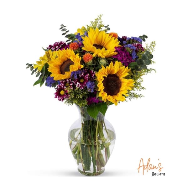 Bouquet of sunflowers and mixed purple flowers in a glass vase